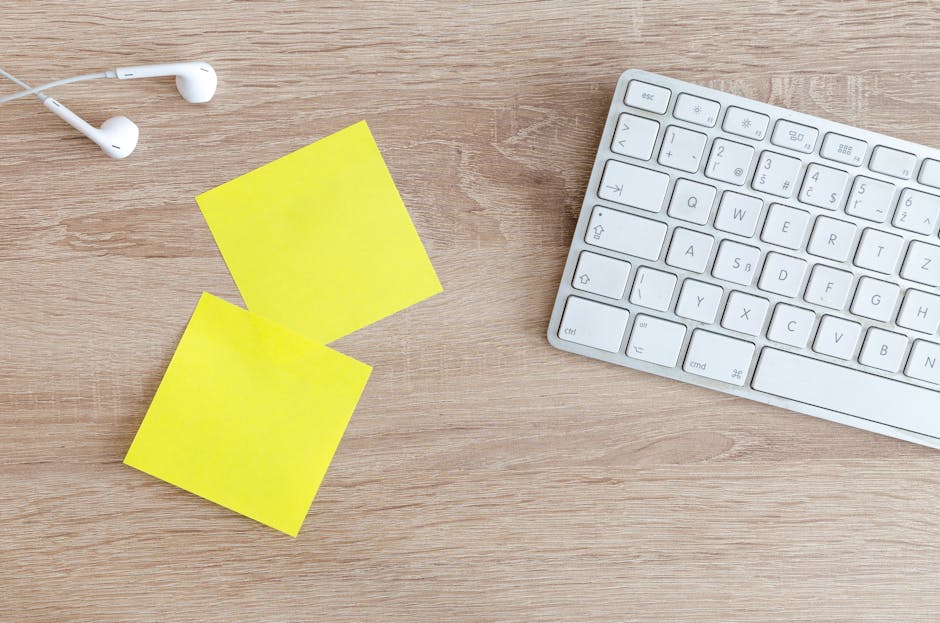 Top view of a workspace with a keyboard, earphones, and yellow sticky notes on a wooden desk