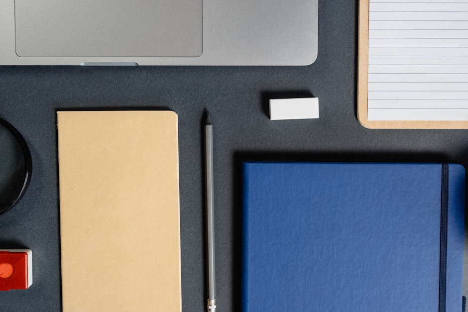 Flat lay of assorted office supplies including notebook, pencil, and laptop on a dark desk